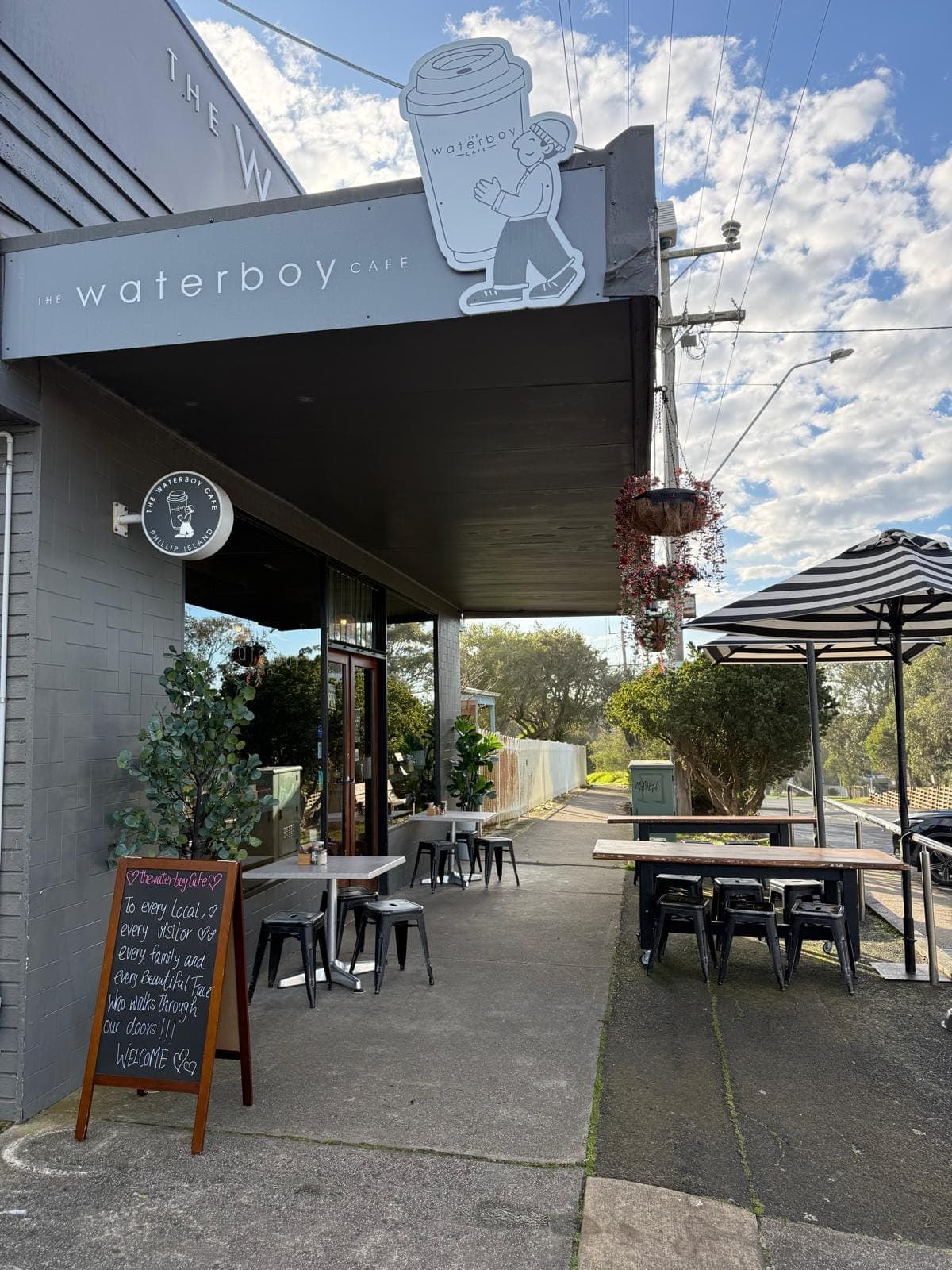 Guests at outdoor cafe tables under a canvas umbrella, shaded by gum trees