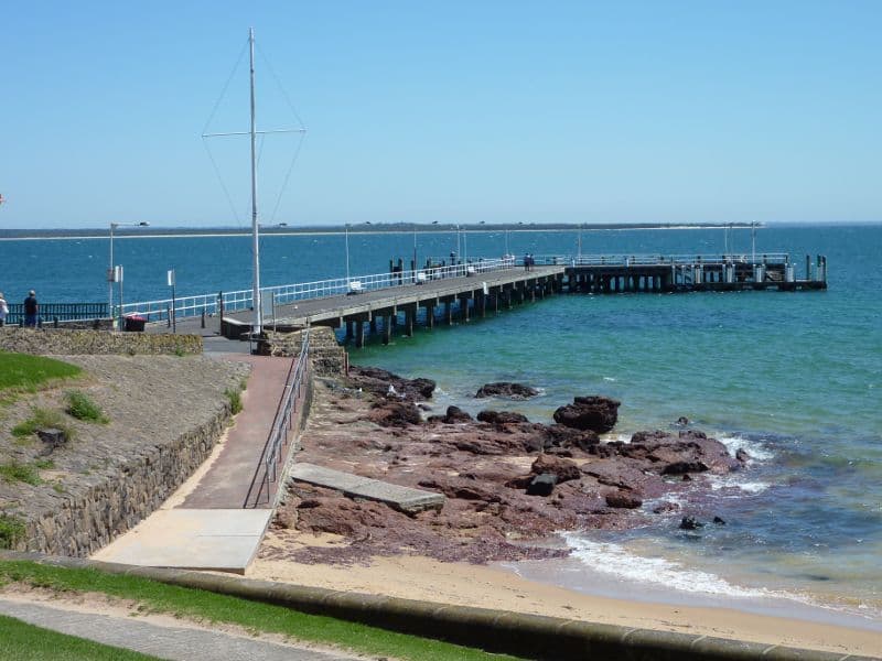 The coastline from above, a long jetty reaching out into calm water past the foreshore
